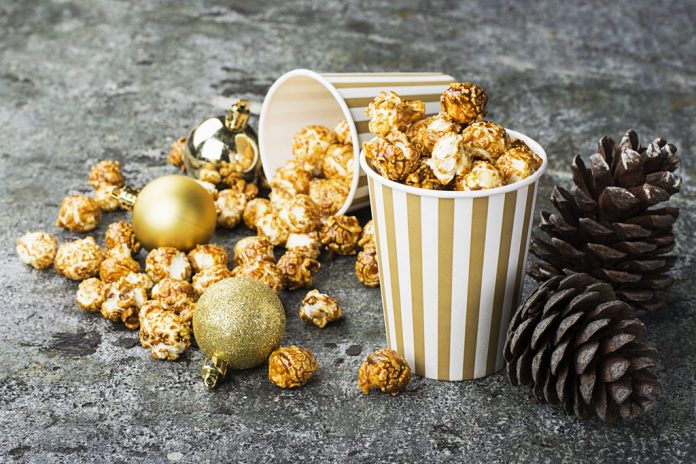 Appetizing golden caramel popcorn in paper striped cups in the New Year's interior with fir cones, New Year's golden balls on a gray stone modern background. Selective focus.