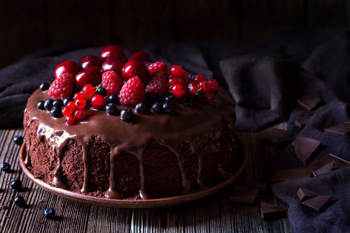 Traditional homemade chocolate cake sweet pastry dessert with brown icing, cherries, raspberry, currant on vintage wooden background.