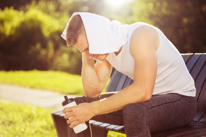 Exhausted man after exercise drinking water and wiping sweat wit